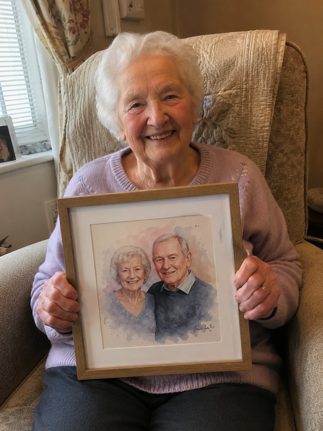 An elderly woman in her armchair beaming as she holds a watercolor portrait of herself and her late husband